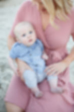 A mother sitting on her knees in the sand looking down at her baby boy in her lap at Ponto beach. 