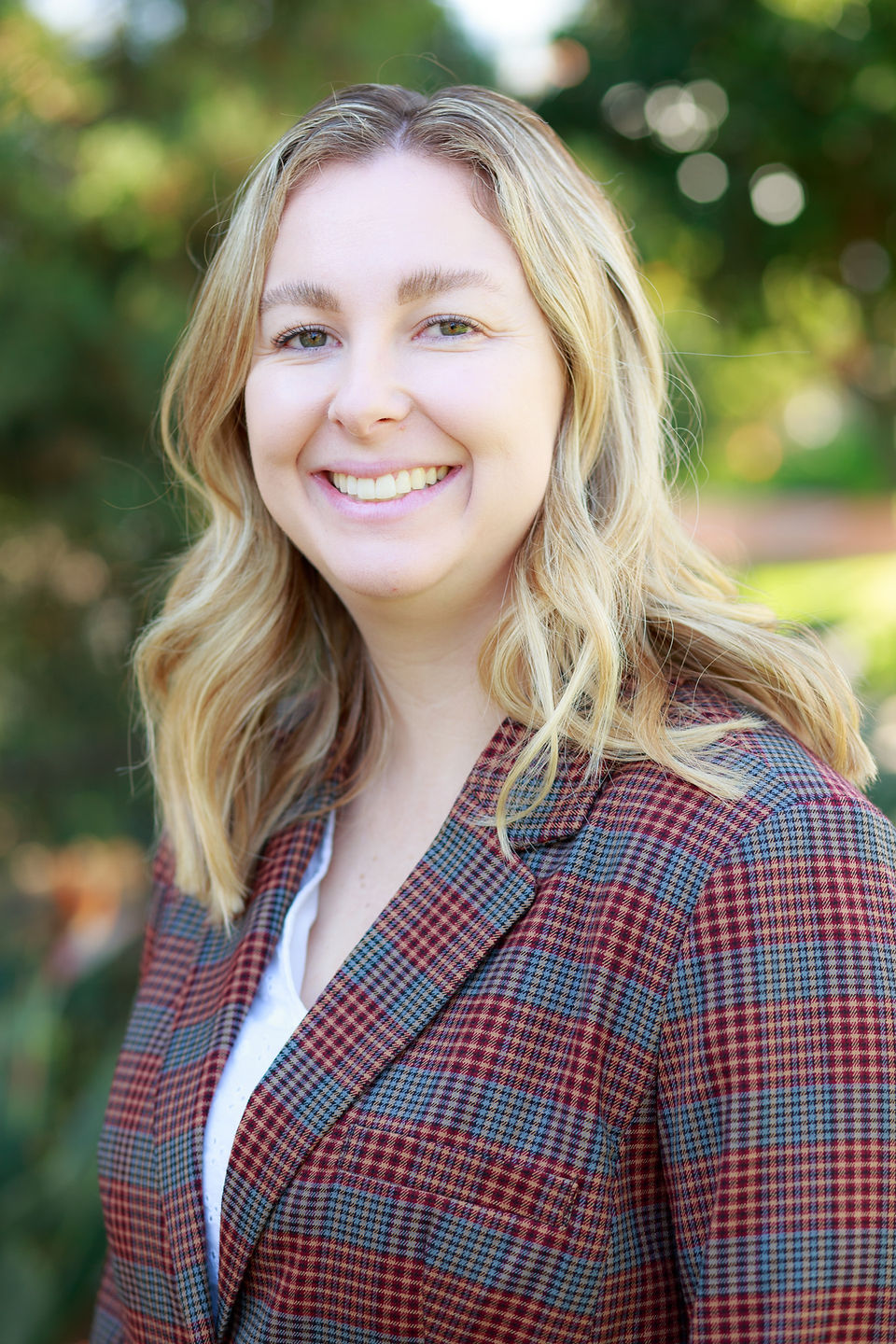 Women with blonde hair, with a plain grey and red blazer and white blouse smiling friendly at camera