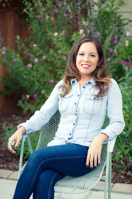 Woman with brown hair sitting in chair wearing dark blue jeans and a pale blue jean type of shirt