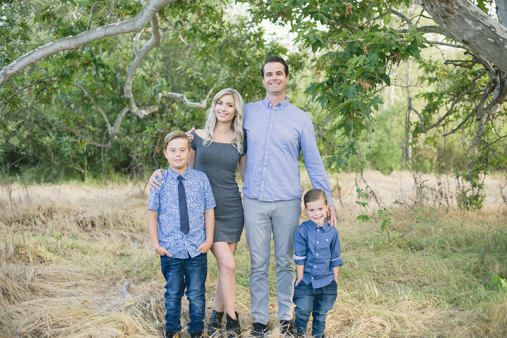 A family poses for a portrait in front of a large tree at Rancho Penasquitos Preserve, smiling together.