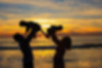 Silhouetted couple lifts children against a colorful sunset on a beach, creating a joyful and warm family moment at Ponto beach, CA