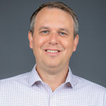 A smiling man in a pink and white checked shirt, part of the executive team headshots in San Diego.