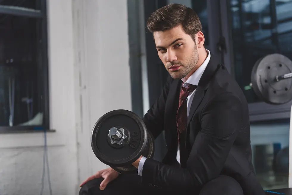 Business professional in a suit lifting a dumbbell in an office gym, symbolizing the balance between mental resilience and physical strength required to scale a business without burning out. Randy Belham, Montreal's best life coach for entrepreneurs, guides leaders in achieving sustainable success through emotional intelligence and well-being.
