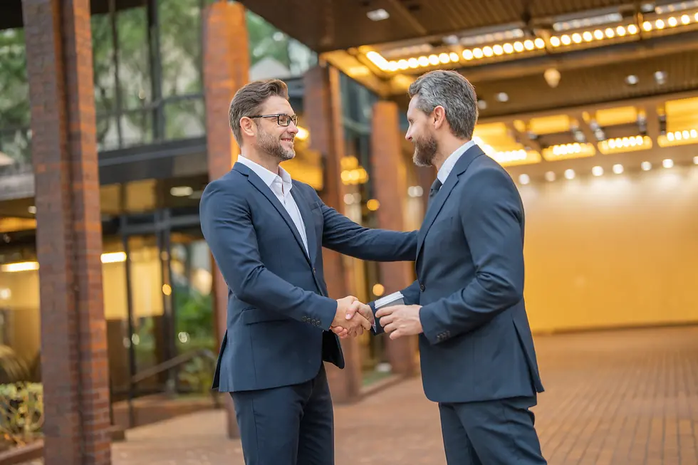 Two business professionals in suits shaking hands and smiling, symbolizing emotionally intelligent leadership built on empathy and authenticity. Randy Belham, Montreal's best life coach for entrepreneurs, emphasizes that leaders who understand and support their teams foster trust, loyalty, and a positive work environment that attracts top talent.