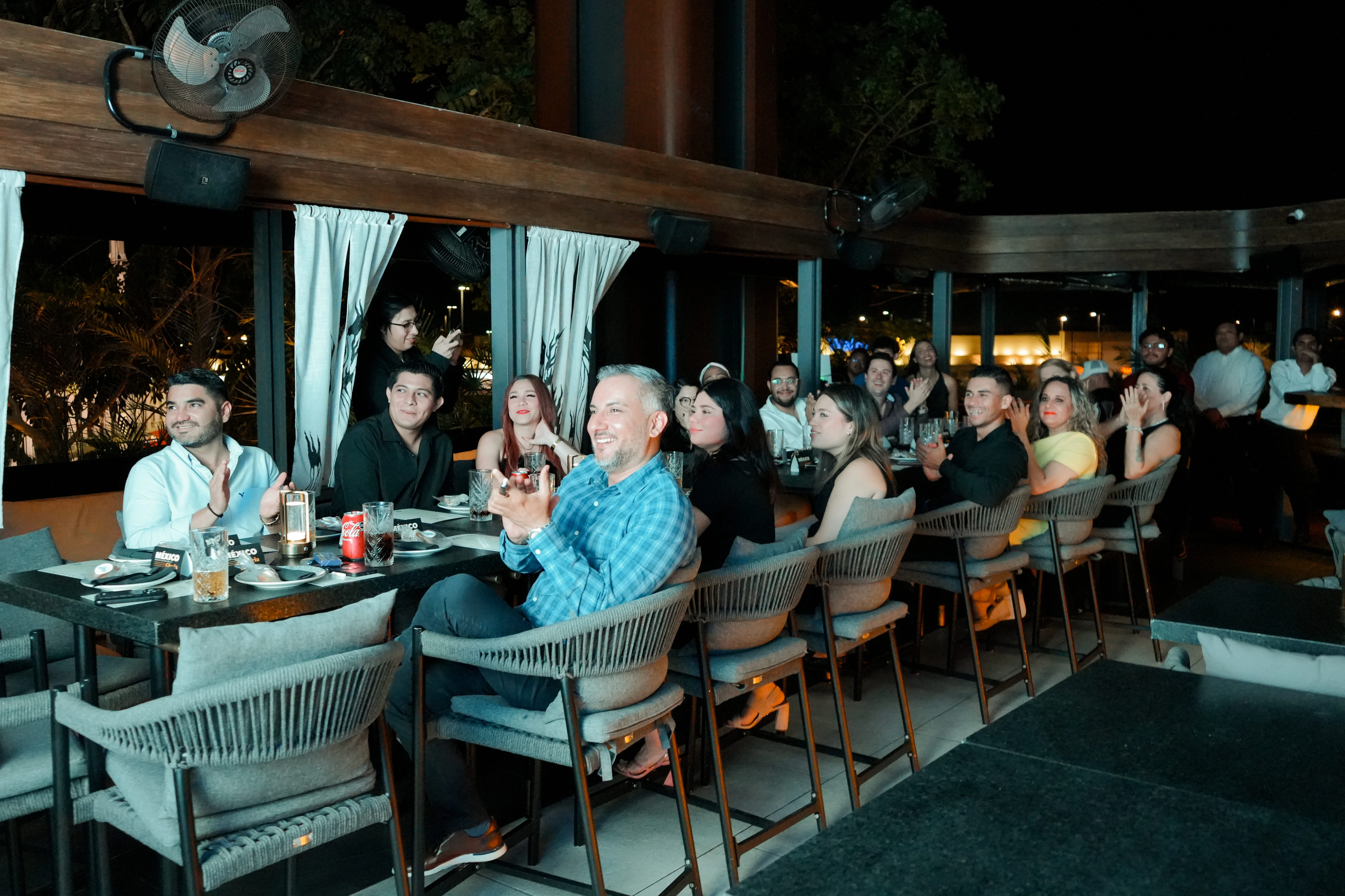 multitud de asistentes de evento aplaudiendo de noche en una mesa larga