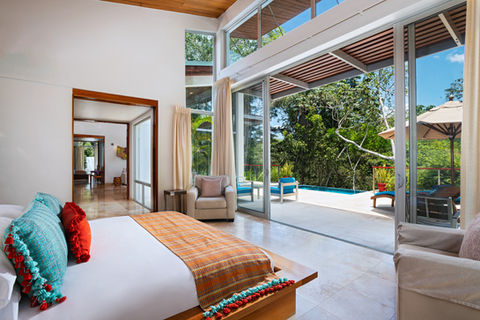 Luxurious bedroom with large glass doors opening to private pool and jungle.