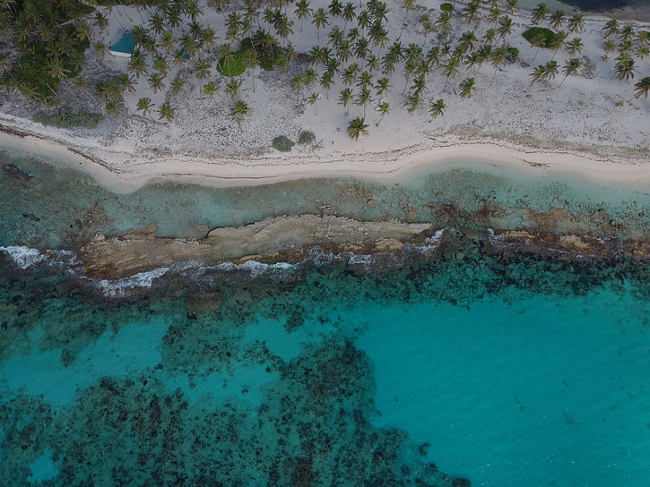 Aerial view tropical sandy beach, turquoise ocean, and underwater rock formations.