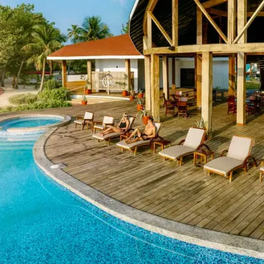 Tourists sunbathing on lounge chairs beside a large resort swimming pool.
