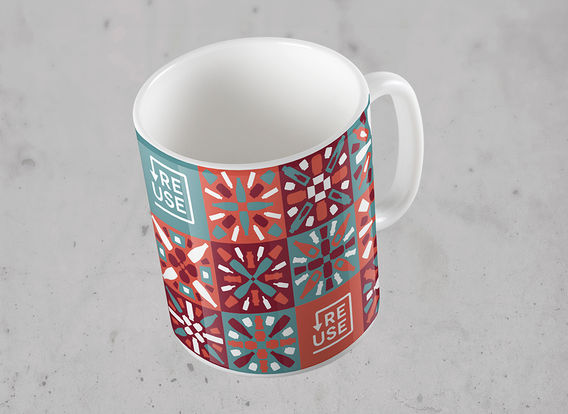 Caneca com o logotipo da Reuse em composição com o padrão de estampa desenvolvido para a marca. As cores utilizadas são marrom, laranja escuro, verde água e branco.