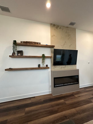 Contemporary fireplace wall with a textured concrete accent, vertical slats, built-in electric fireplace, and rustic floating wood shelves in Nocatee, Atlantic Beach, and Avondale homes.
