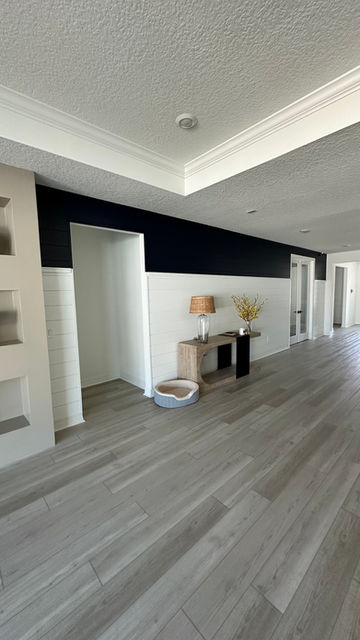 This transitional-style accent wall by AVP Construction JAX features white horizontal shiplap paired with a bold navy upper section, creating a striking two-tone design in a bright, open hallway. Finished with crisp white trim, clean baseboards, and elegant crown molding, this space showcases expert interior trim work and precision finish carpentry. The modern light wood console, recessed niches, and luxury vinyl plank flooring enhance the overall sophistication. Perfect for homeowners in Jacksonville, FL looking to elevate their interiors with custom shiplap walls, crown molding, and contemporary wall treatments.