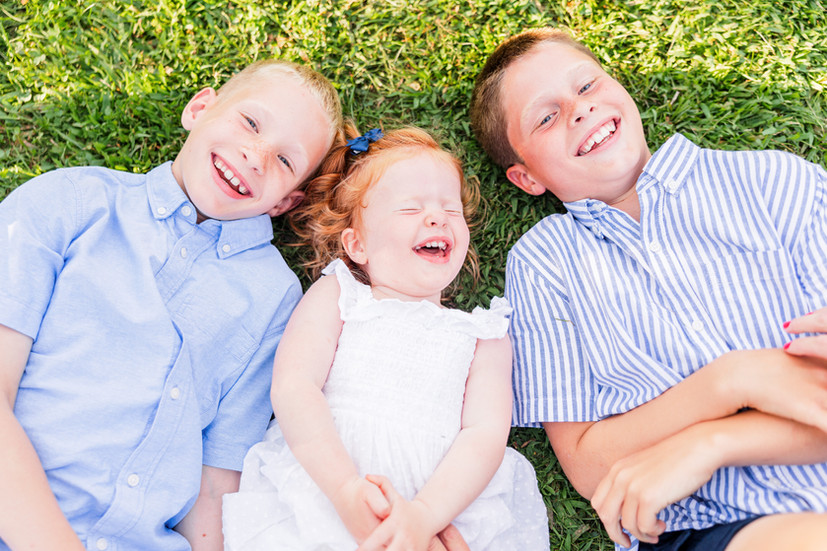 Three siblings laying in grass laughing