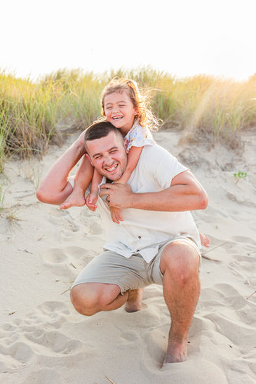 Father giving his daughter a playful piggyback ride on the beach during a Virginia Beach family portrait session