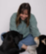 Bre, a studio and outdoor pet photographer, smiles at her dogs Isla and Roux laying in front of her at a studio session.