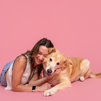 Woman and dog lay on their stomachs posing in front of a pink studio backdrop.