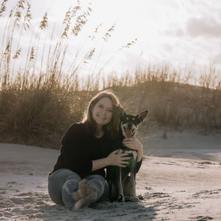Woman and dog sit on the sand at Wrightsville Beach during the months of October - March for a beach pet photo session.