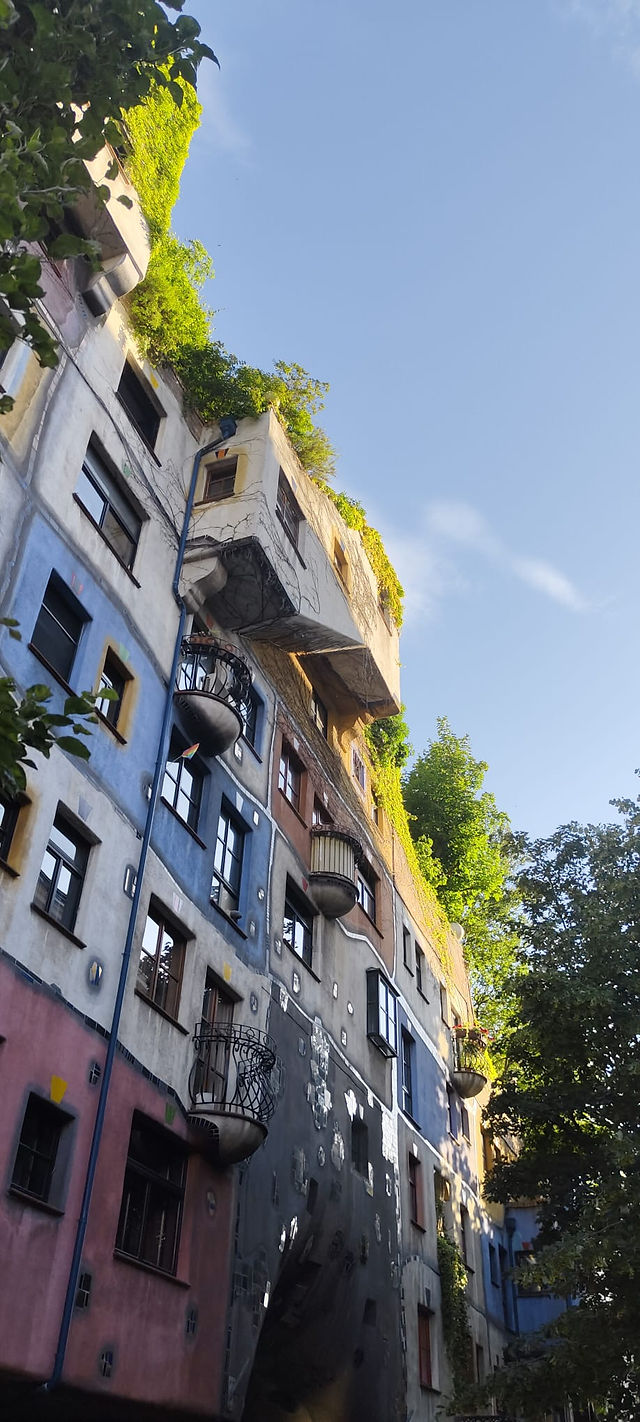 Színes, hullámos homlokzatú épület zöld tetővel és kék ég a háttérben.