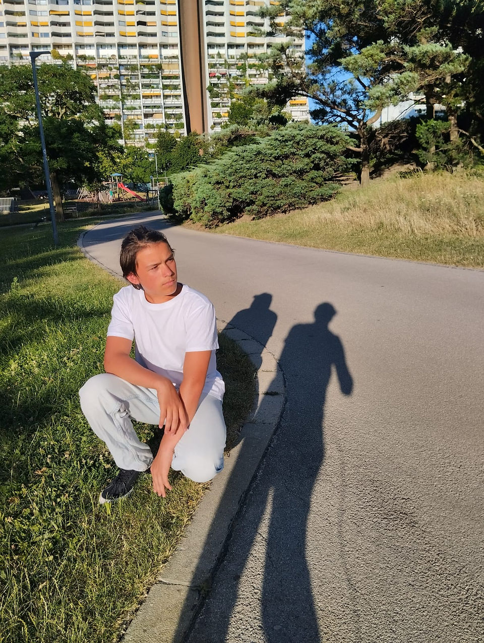 Fiatal férfi a zöld fűben, fehér pólóban és farmerben, napfényes környezetben.