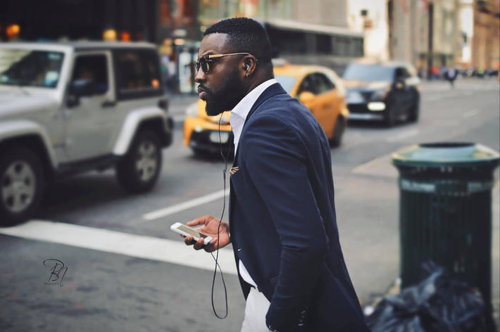 Stílusos férfi sétál az utcán, telefont tart, elegáns öltözékben, napszemüvegben. Bánhalmi Norbert fotókiállítás Tihany