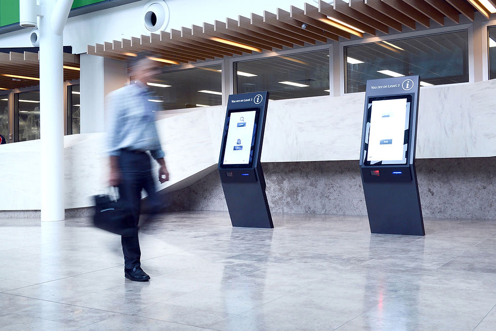 Man walking past digital kiosks displaying "Welcome" and building information.