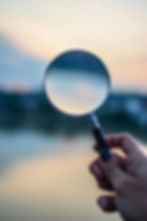 Hand holding a magnifying glass against a blurred sunset background. Soft pastel colors with a focused view through the glass.