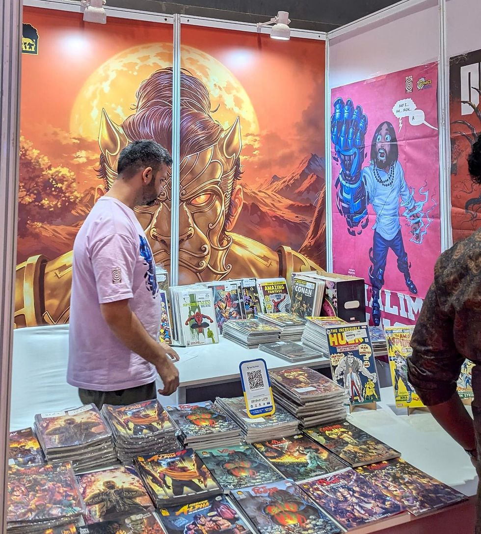 Man browsing comics at a booth with a large golden mask mural. Colorful comics are stacked on a table. Bright and lively atmosphere.