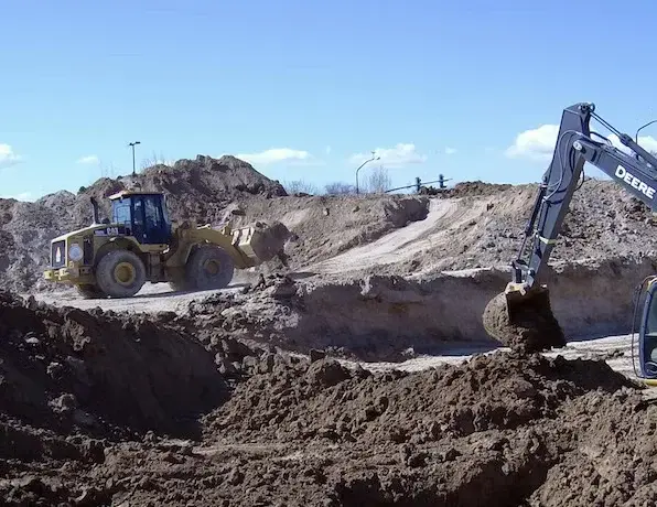Heavy machinery excavating dirt at an active construction site development under a clear blue sky