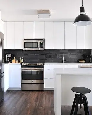 Contemporary kitchen with glossy white cabinets, stainless steel appliances, and a black subway tile backsplash in a newly remodeled home.