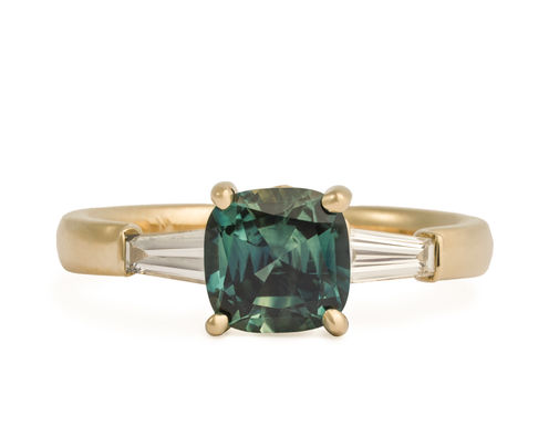 Top view of three stone yellow gold ring with blue-green sapphire center stone and tapered diamond baguette side stones.