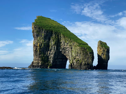 Imponente arco naturale di roccia basaltica ricoperto di erba verde nelle Isole Faroe