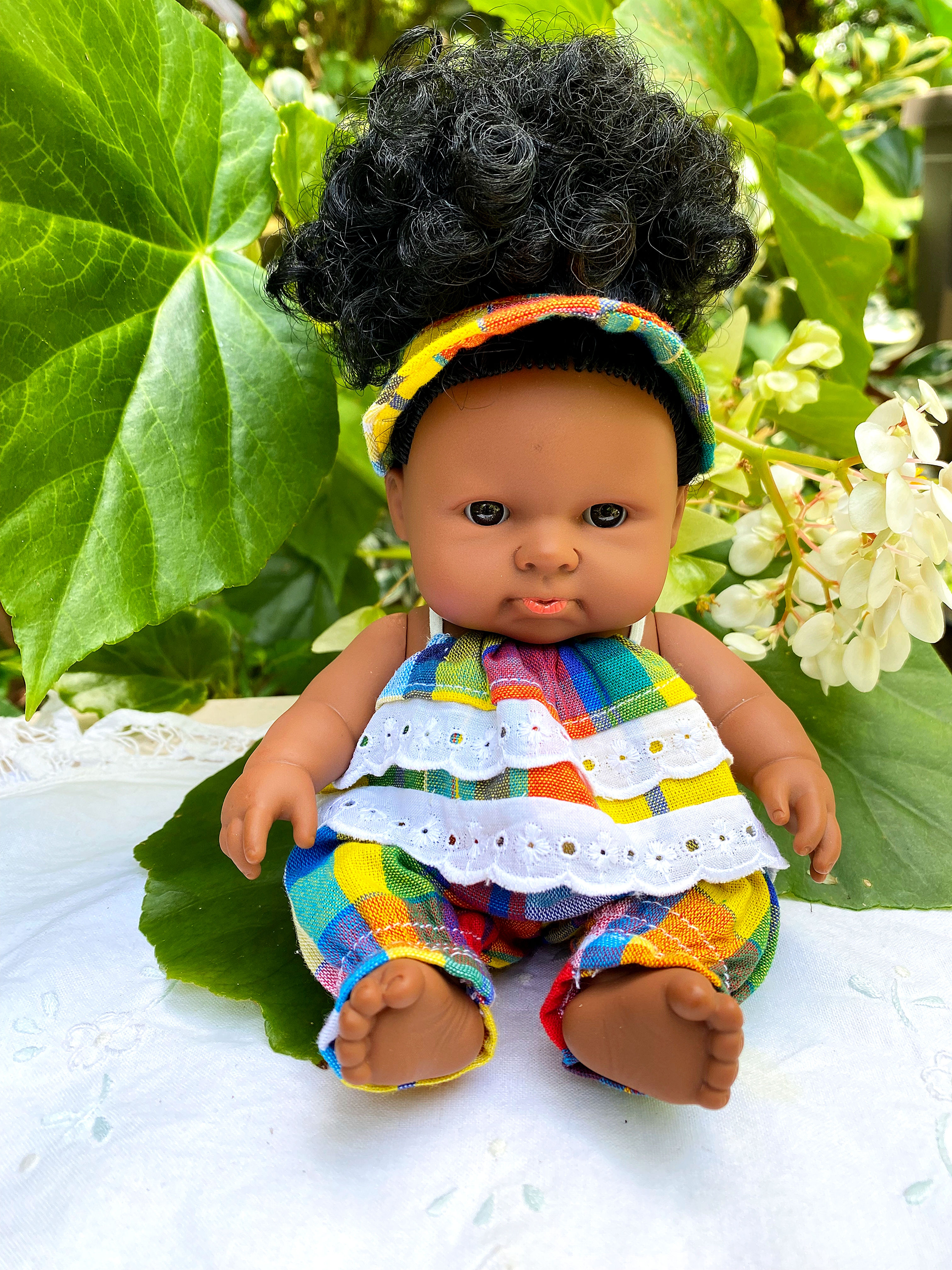 Poupée en barboteuse madras colorée avec visière assortie et volants brodés, posée sur un fond tropical en Martinique