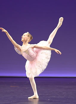 Ballet dancer in a pink and white tutu performing an arabesque en pointe on stage