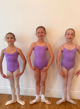 Three young MV Academy ballet students in lilac leotards and pink ballet shoes standing in first position