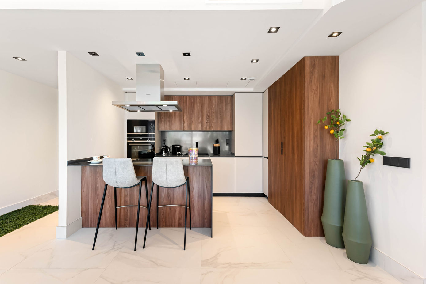 modern kitchen with island and bar chairs and large green floor vases with lemontree branches inside