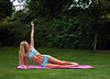 Woman in blue activewear performing a side plank on a pink mat in a lush green garden, arm raised, serene expression.