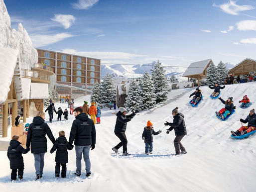 People in winter clothes enjoy snowy slopes, sledding and playing. Snowy trees and buildings in background, clear blue sky above.