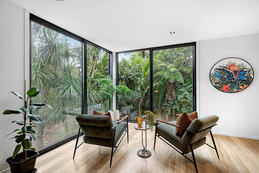 Stylish staged lounge in Mt Eden, Auckland with modern armchairs, indoor plants, and large windows overlooking lush greenery.