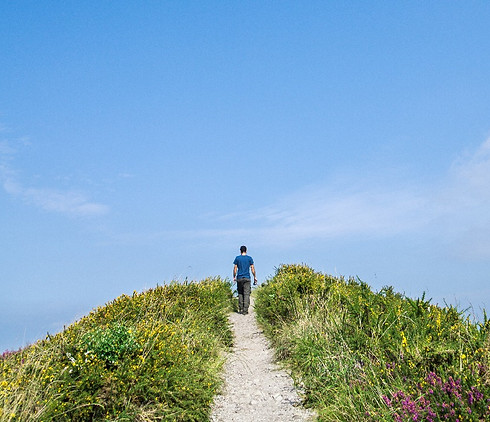 Man walking up trail with big blue sky