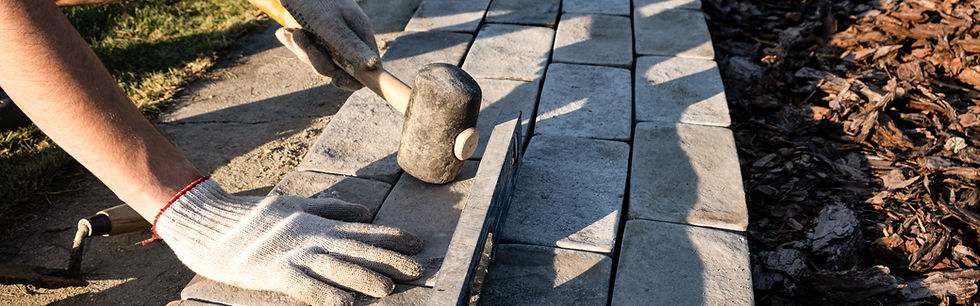 Worker using a mallet to lay stone pavers for a walkway.