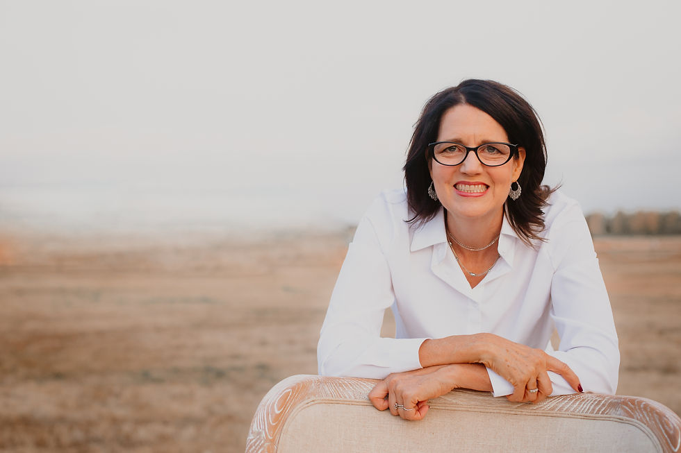 Picture of tall white woman with brown hair and glasses in front of a desert scene.