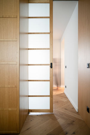 view trough a sliding door with stunning glass elements that allow for diffused light to flow seamlessly between the rooms. a japandi livingroom with heringbone oak parquet