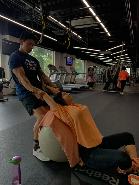 Woman getting a post workout deep stretching by personal trainer using a medicine ball.