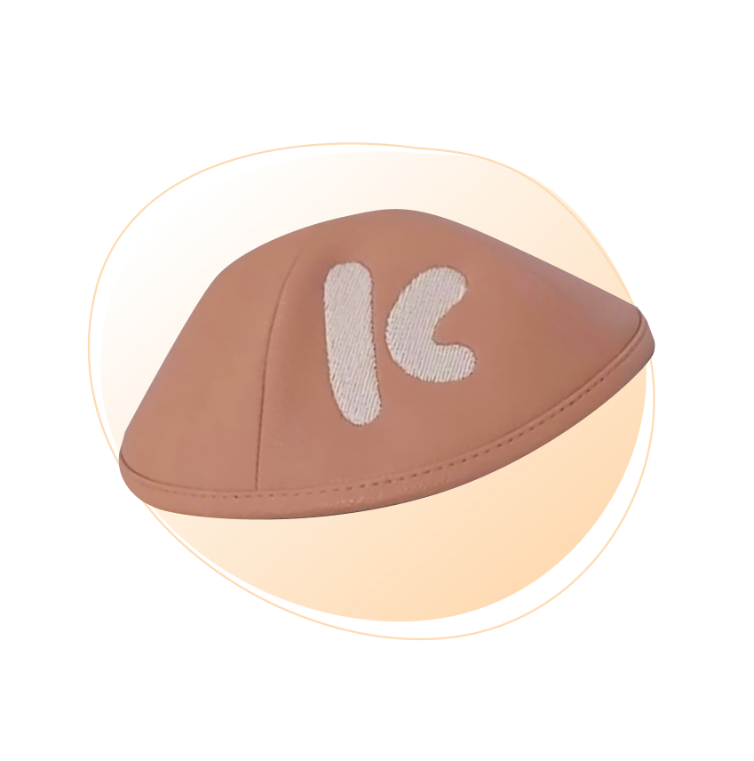 A plain brown kippah with large light brown filled letter embroidered on the front,