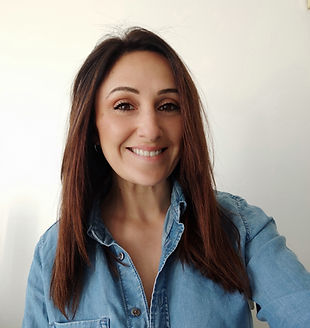 Photo d'une femme souriante, portant une chemise en jean, avec les cheveux bruns lâchés, posant devant un fond neutre