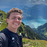 Robert Dobai smiling on a Swiss mountain summit in a trail vest, a lake far below