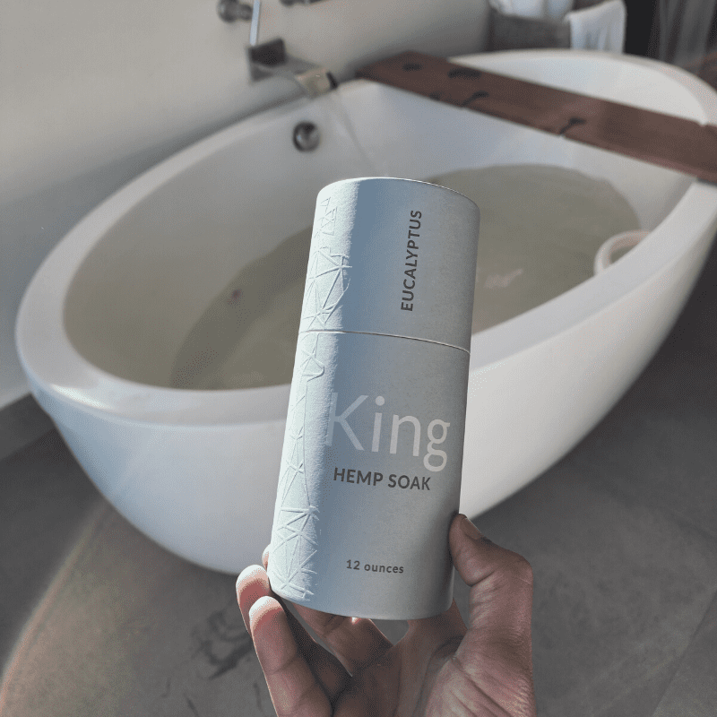 A hand holding the King Soak by Unplugged Essentials while the water is running behind it for his bath.
