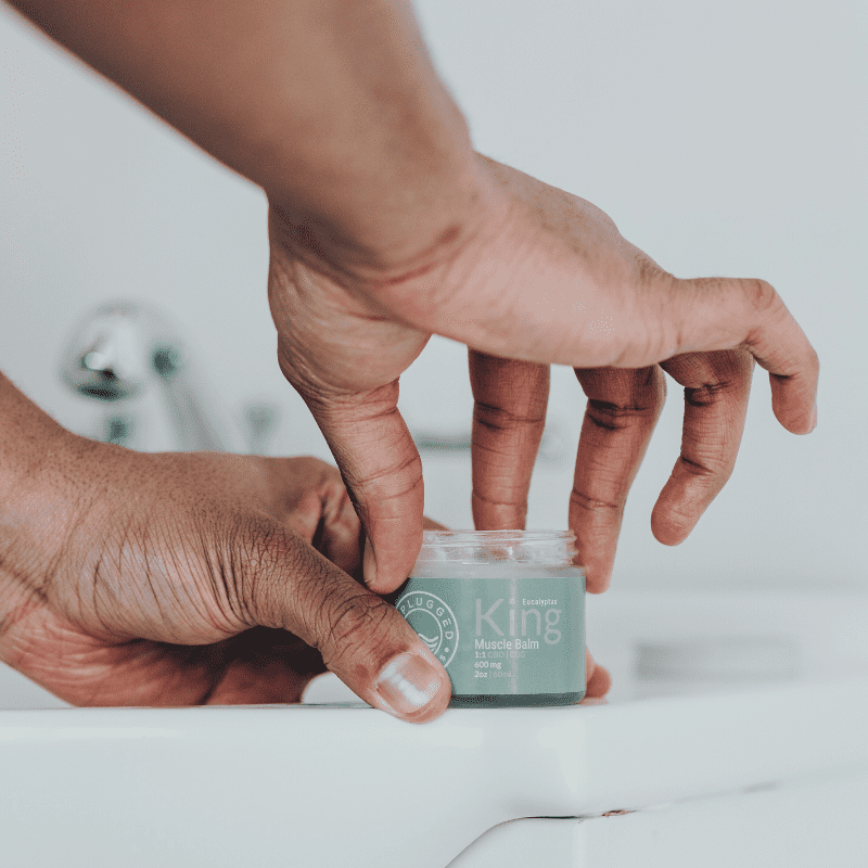 Hands dipping into the container of the King Muscle Balm.
