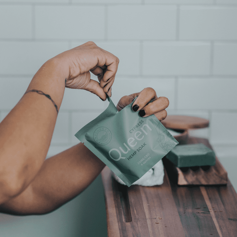 A woman in a bath tearing the packaging on the Queen Soak in 4 ounces.