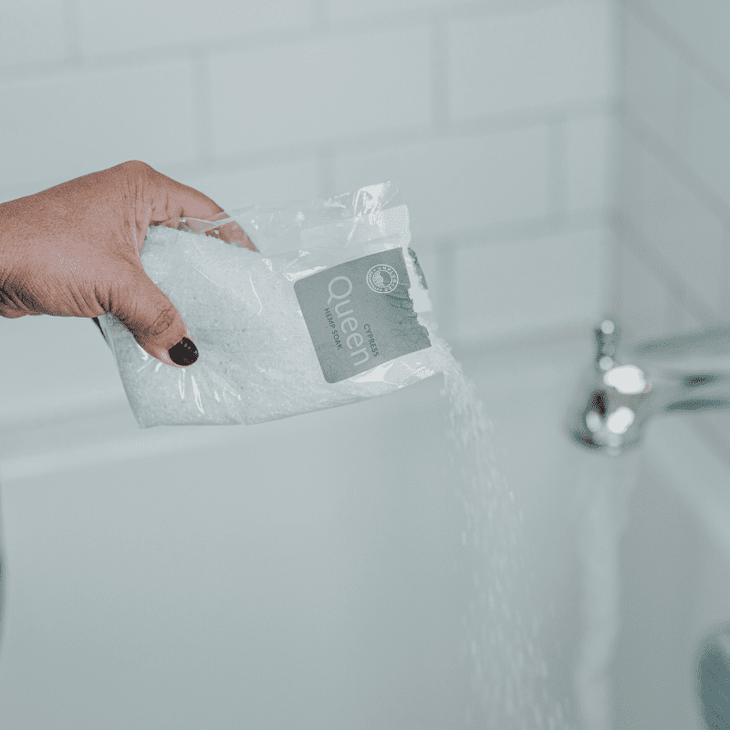 A hand pouring in the interior packaging of the Queen soak into a running bath.