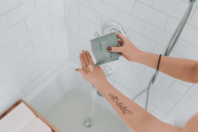Hand pouring a handful of Unplugged Essentials Knight Soak in a bath with running water.